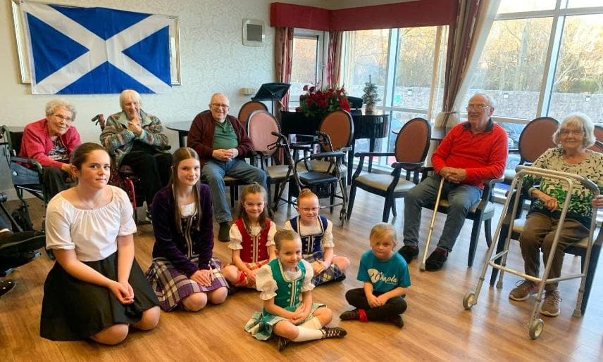 Young traditional Scottish dancers sitting with care home residents
